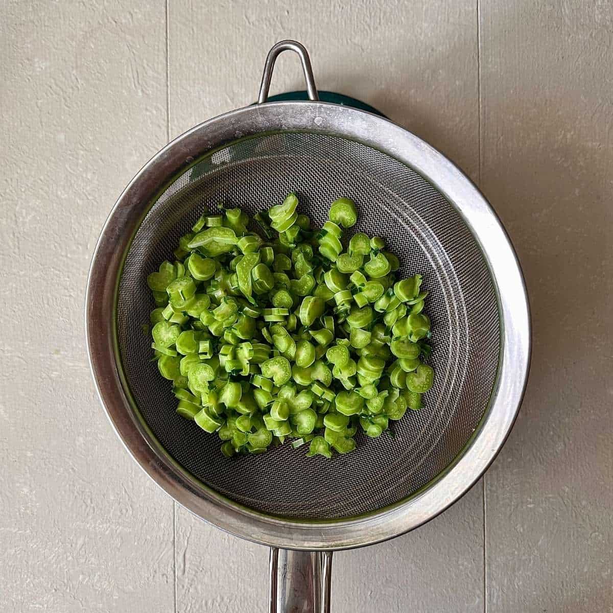 Evenly chopped kale stem in a colander that sits in s saucepan. For smashed edamame toast recipe.