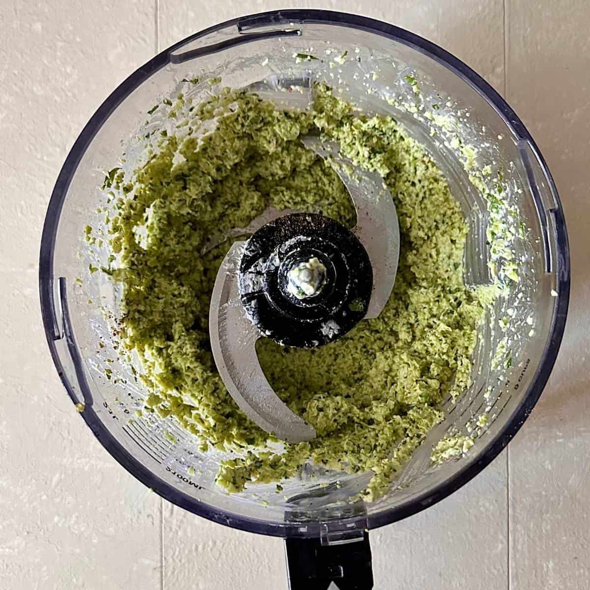 A large blender jug containing blended kale stems, edamame beans, garlic, lemon juice, cream cheese, olive oil, salt and pepper for smashed edamame toast.