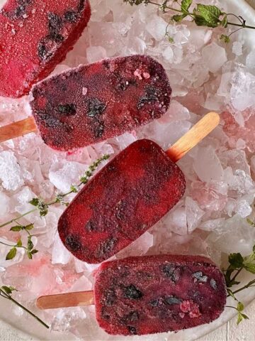 Four rose and basil seed popsicles displayed in a bowl of crushed ice.