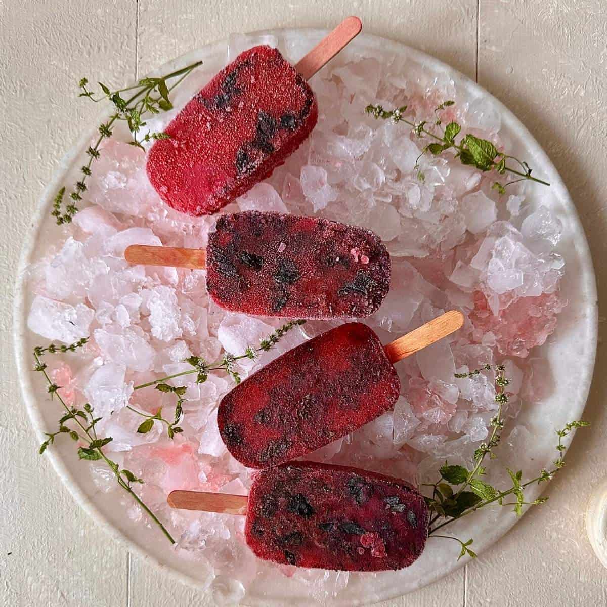 four frozen rose and basil seed popsicles on a bed of ice on a plate.
