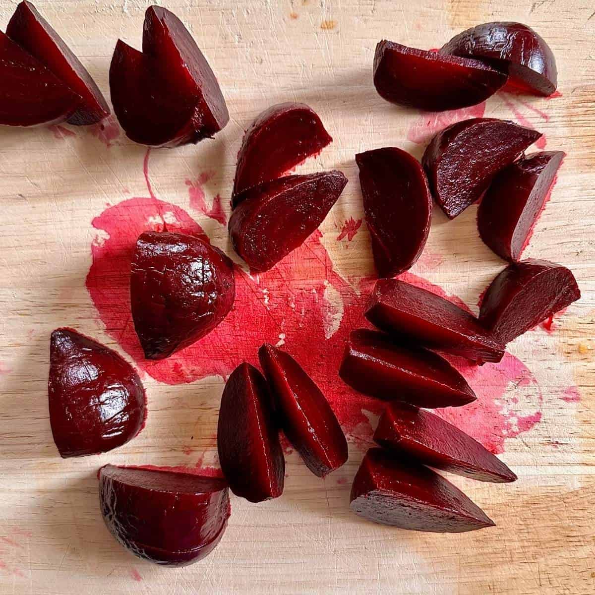 Cooked beetroot on a wooden chopping board, cut into bite-sized wedges for beetroot, peach and feta salad.