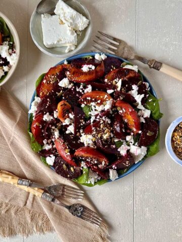 Beetroot and peach salad with feta cheese, baby spinach and toasted seeds on a blue plate.