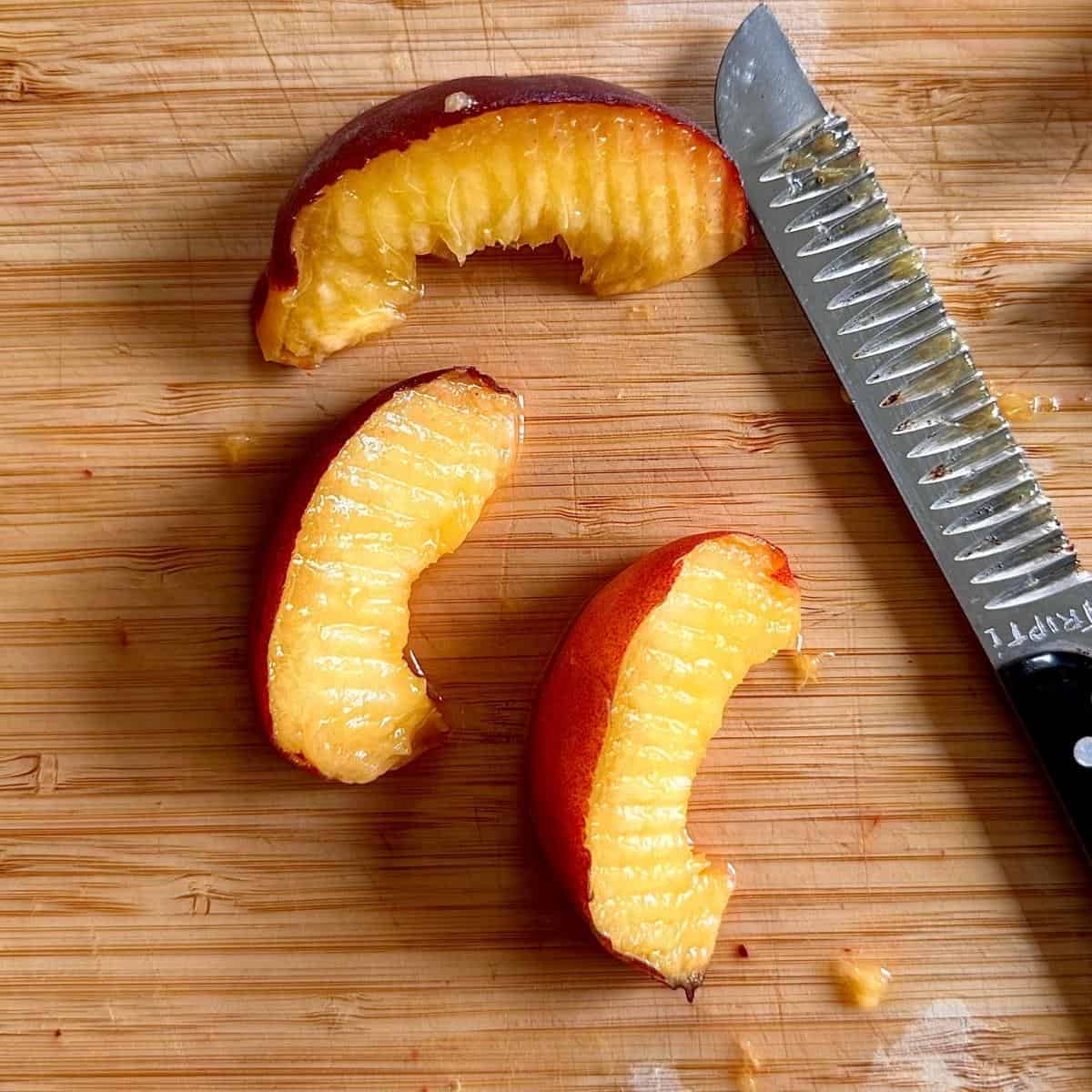 Peach wedges on a wooden chopping board for beetroot, peach and feta salad. The peaches have been cut with a ridged knife to produce a ridged surface on the peach slices.