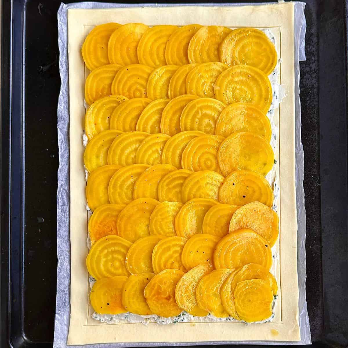 thin slices of golden beetroot layered on top a layer mascarpone cheese with chives and puff pastry, ready to bake. For beetroot tart recipe.