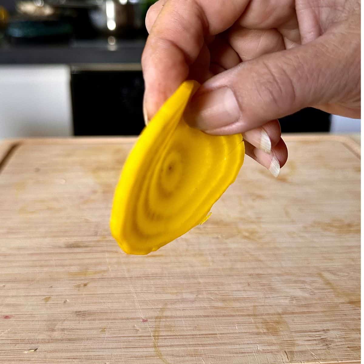 Close-up of a hand holding a thin slice of golden beetroot to show thickness. For a beetroot tart recipe.