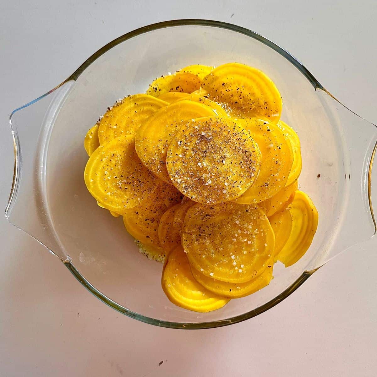 A glass dish containing thin golden beetroot slices, marinated in lemon juice and salt. For a beetroot tart recipe.