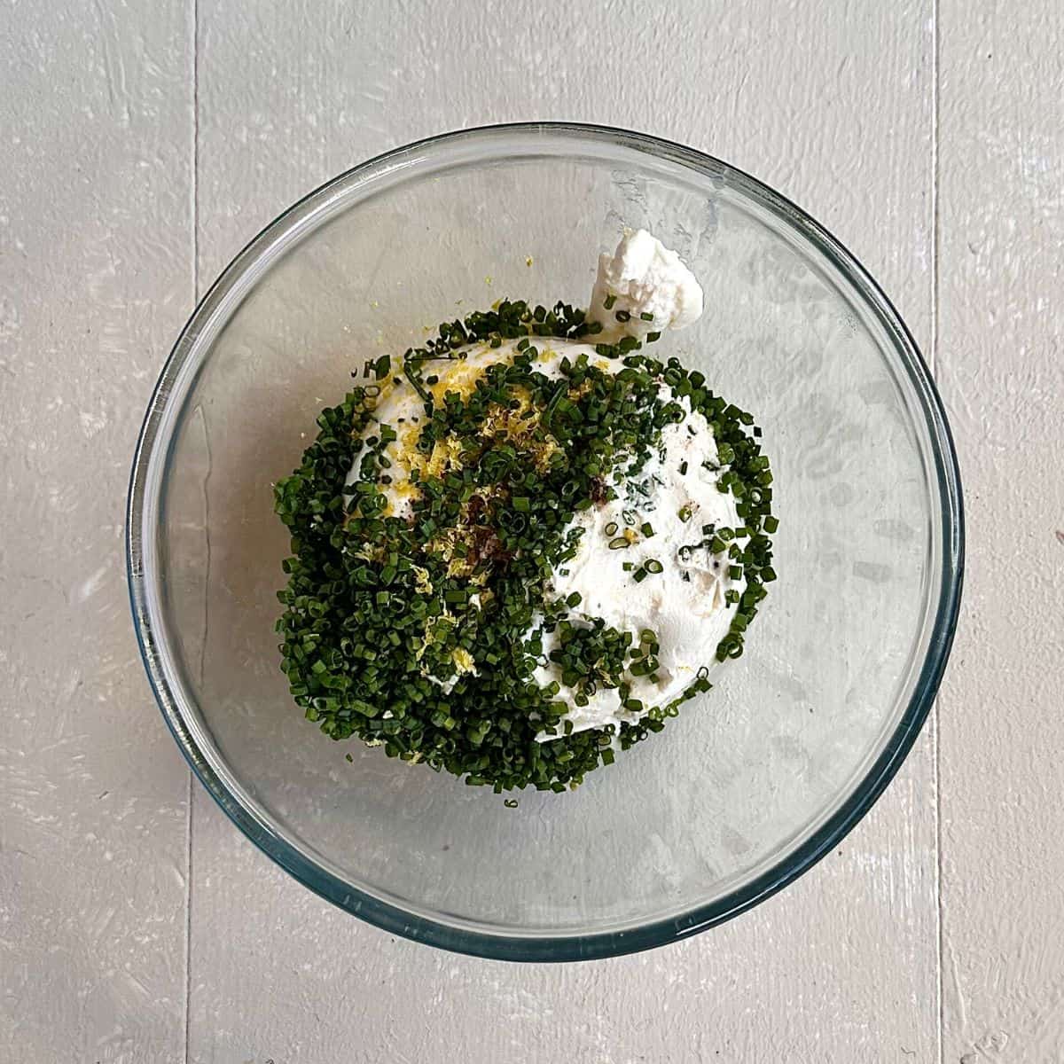 A glass bowl containing mascarpone cheese, finely chopped chives, lemon juice and olive oil, for a beetroot tart recipe.
