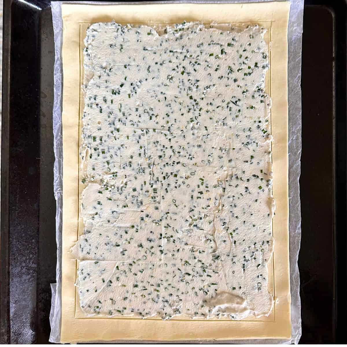 A layer of mascarpone cheese and chives spread onto a sheet of puff pastry for a beetroot tart recipe.