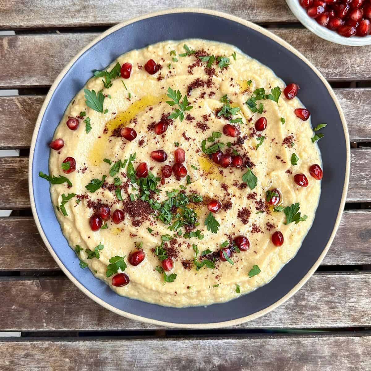 A serving plate containing courgette moutabbal, garnished with sumac, parsley and pomegranate.