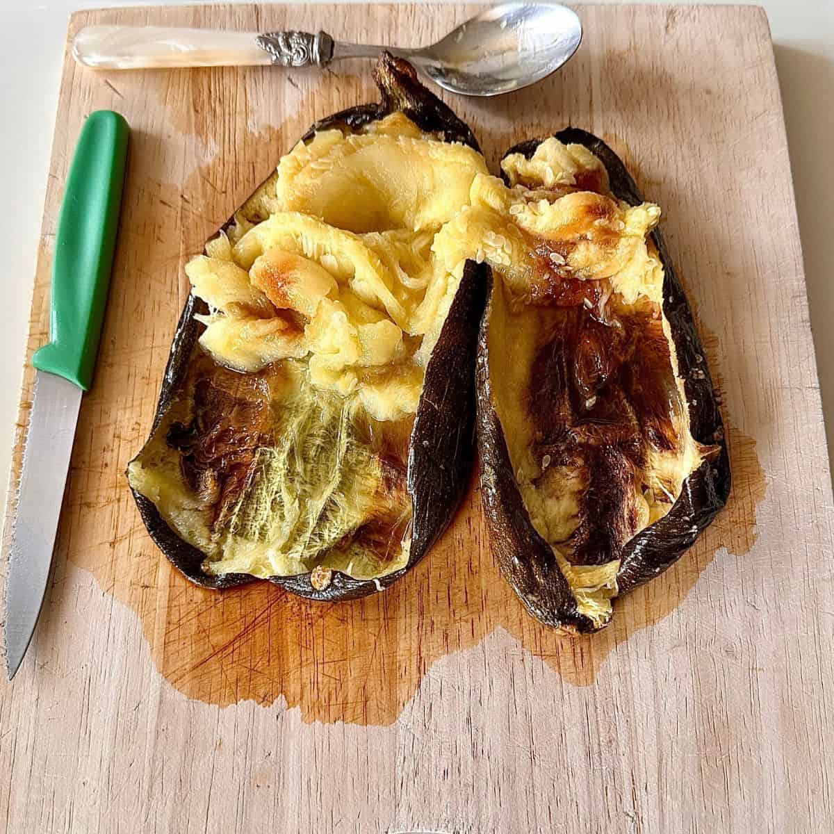 A chopping board with two baked courgettes cut in half. The flesh inside has been scraped to one end, ready to transfer to a blender. For courgette moutabbal.