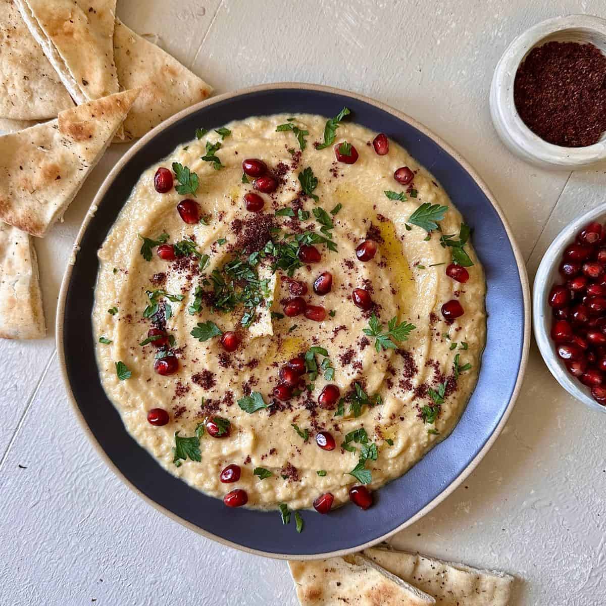 A plate spread with courgette moutabbal, a courgette dip, garnished with pomegranate, parsley and sumac.