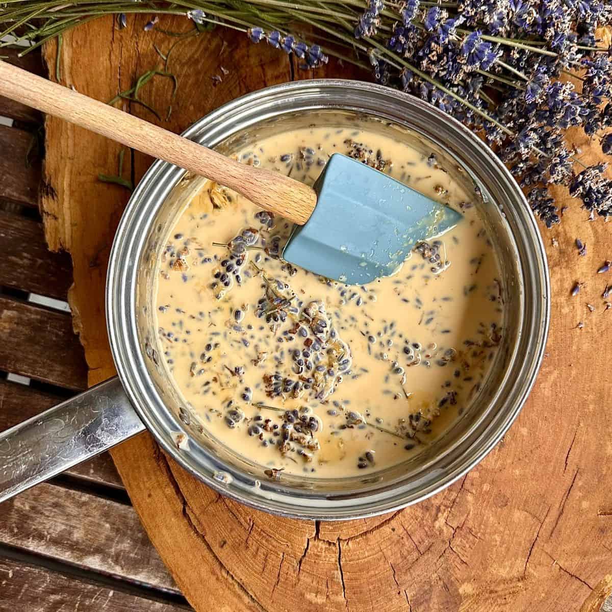 A steel saucepan containing evaporated milk with lavender flowers infusing in it for elderberry lavender ice cream.
