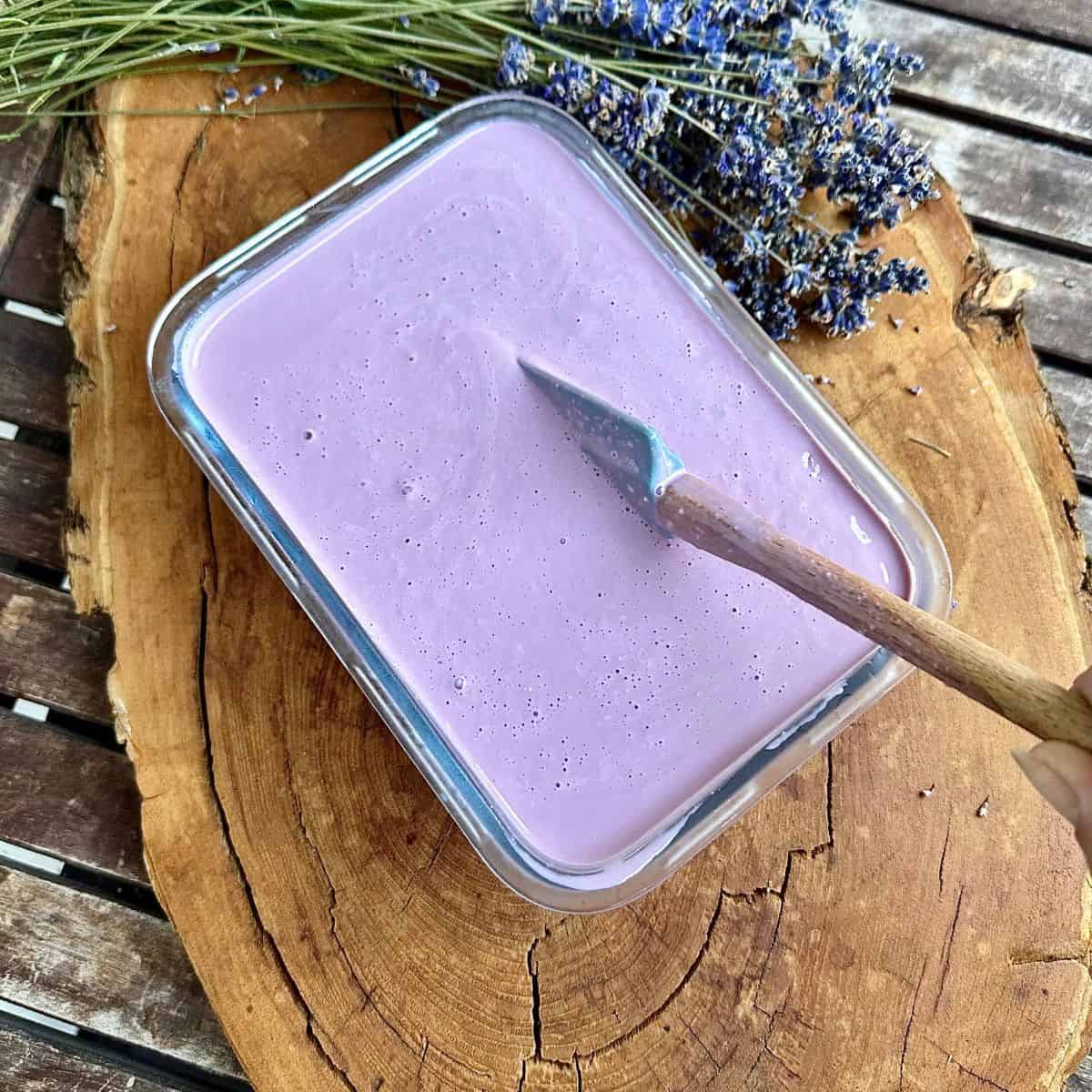 Elderberry lavender ice cream in a glass dish after two hours freezing. A spatular sits in the ice cream to stir it.