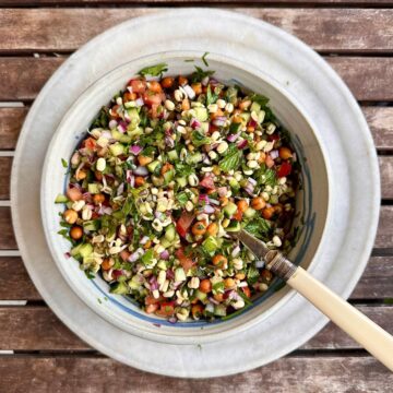 Bowl on a plate containing kachumber salad with kala chana and green mung bean sprouts. A spoon sits in the bowl.