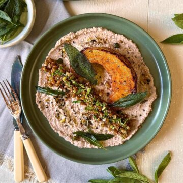 Roasted pumpkin on black-eyed pea hummus with spelt, herbs, seeds and crispy sage. On a green plate.