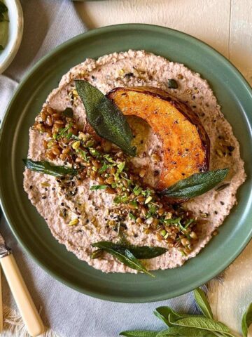 Roasted pumpkin on black-eyed pea hummus with spelt, herbs, seeds and crispy sage. On a green plate.