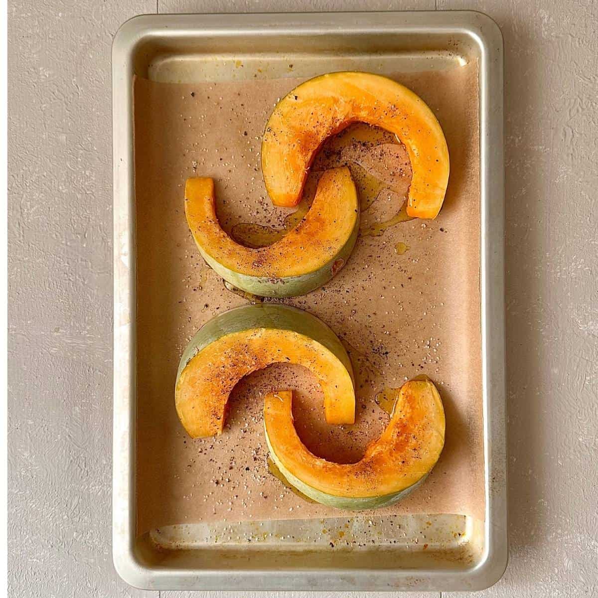 A baking tray lined with parchment paper with four wedges of crown prince pumpkin seasoned with salt and pepper and drizzled with olive oil. For roasted pumpkin black eyed pea hummus