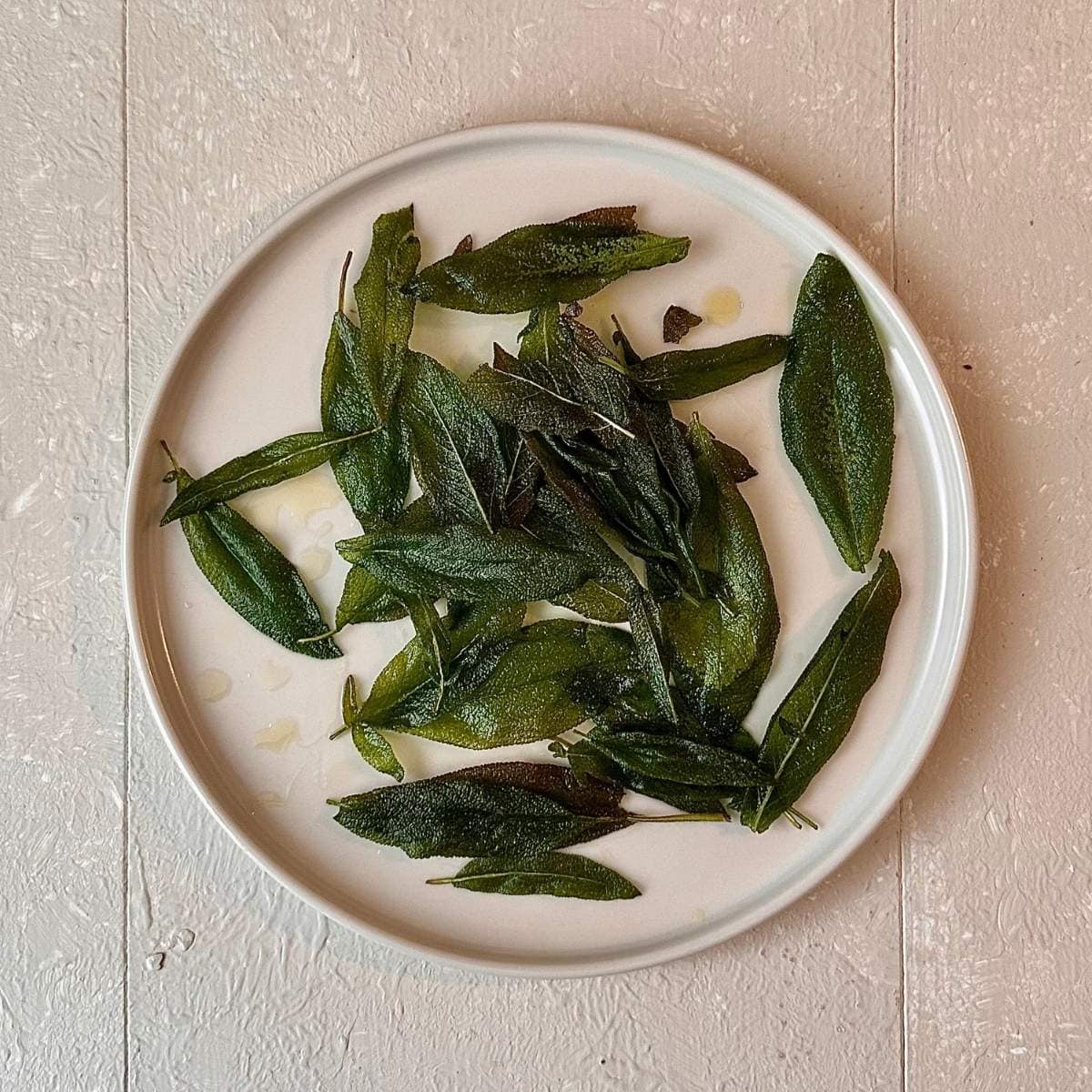 A beige coloured plate containing fried sage leaves for roasted pumpkin and black eyed pea hummus recipe.