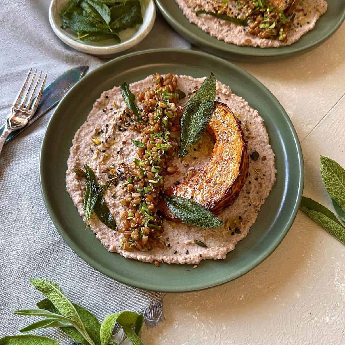 Roasted pumpkin sits atop creamy black-eyed pea hummus with herbs, seeds, and crispy sage. All on a green plate.