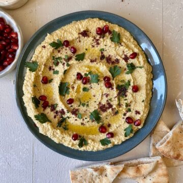 A blue plate spread with watermelon rind hummus, garnished with sumac, parsley and pomegranate seeds.
