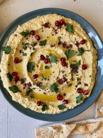A blue plate spread with watermelon rind hummus, garnished with sumac, parsley and pomegranate seeds.