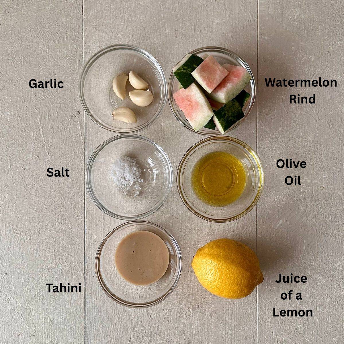 Ingredients for watermelon rind hummus recipe laid out on a white background in small glass dishes. The ingredients are annotated.