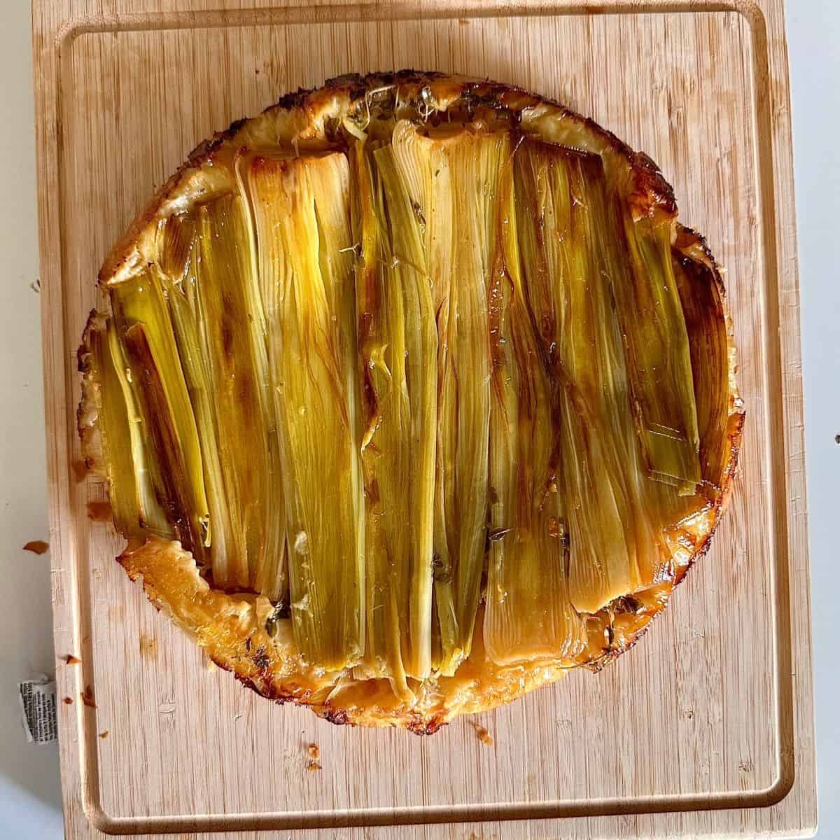 A leek tarte tatin on a wooden chopping board after baking.