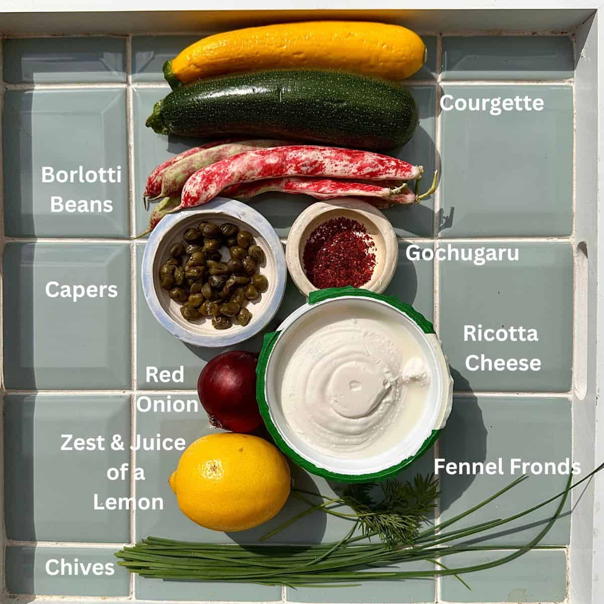 Ingredients for ribboned courgette salad laid out onto a green tile background. The ingredients are annotated.