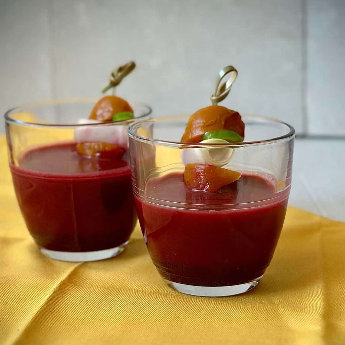 Two glasses containing beetroot aguachile with beetroot and cucumber skewers.