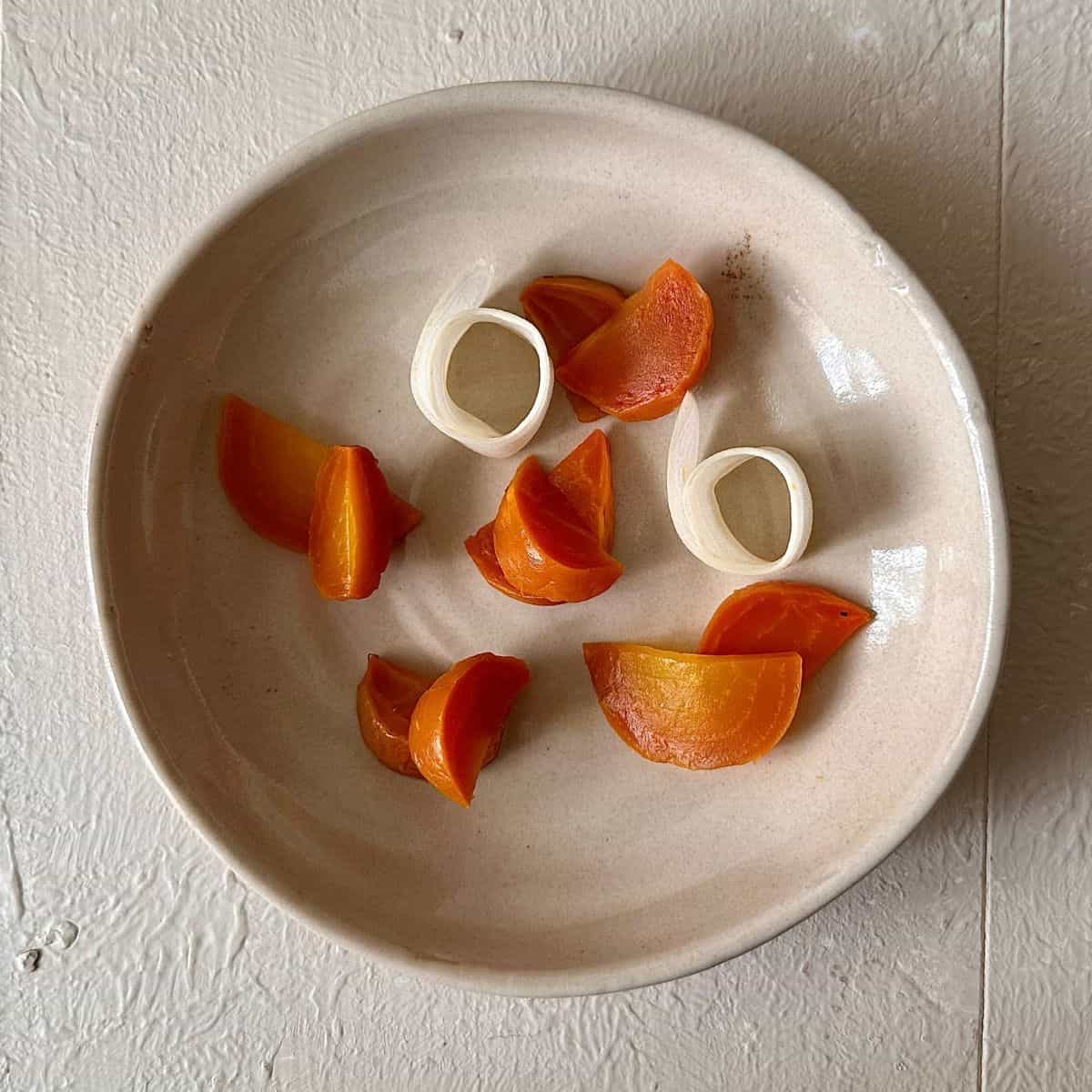 A beige bowl containing ribbons of cucumber and wedges of cooked golden beetroot. Garnish for beetroot aguachile recipe.