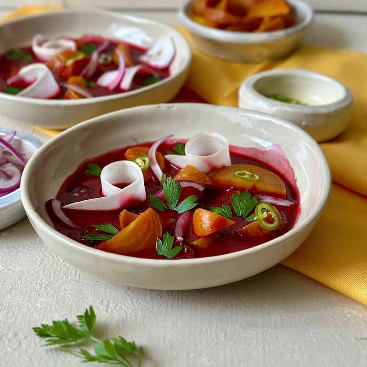 A bowl of beetroot aguachile garnished with cucumber ribbons, roasted golden beetroot wedges, coriander leaves and chilli slices.