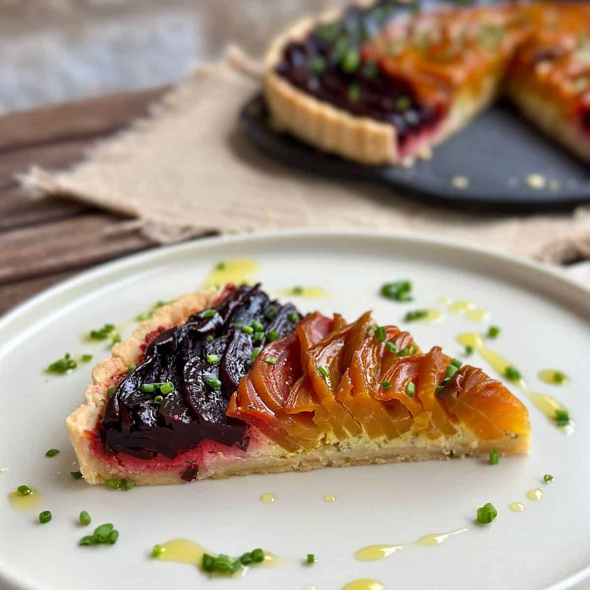 A slice of beetroot and goats cheese tart, showing the beetroot/goats cheese layers. The whole tart sits on a serving plate in the background