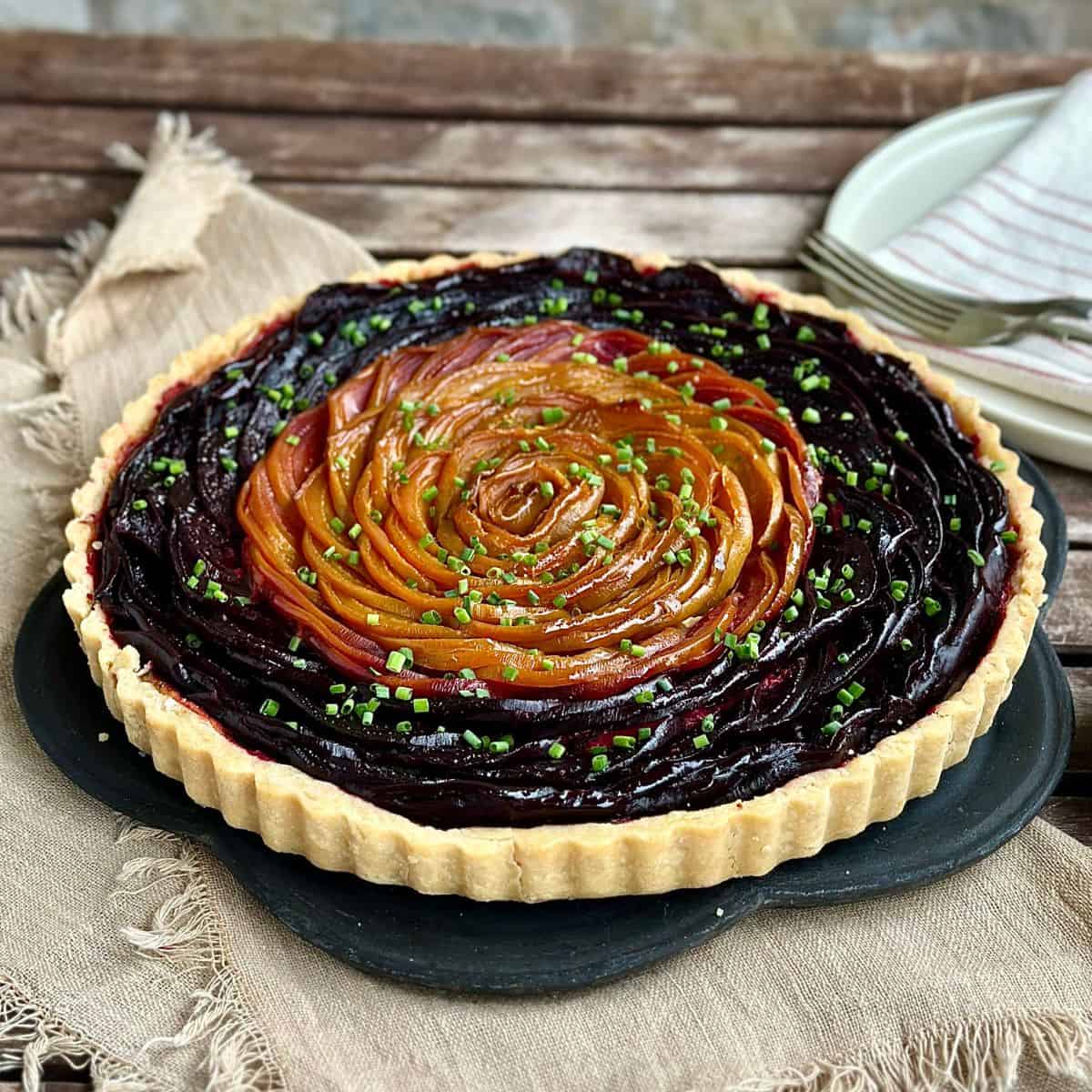 A baked beetroot and goats cheese tart garnishes with finely chopped chives, sitting on a slate plate, ready to serve.