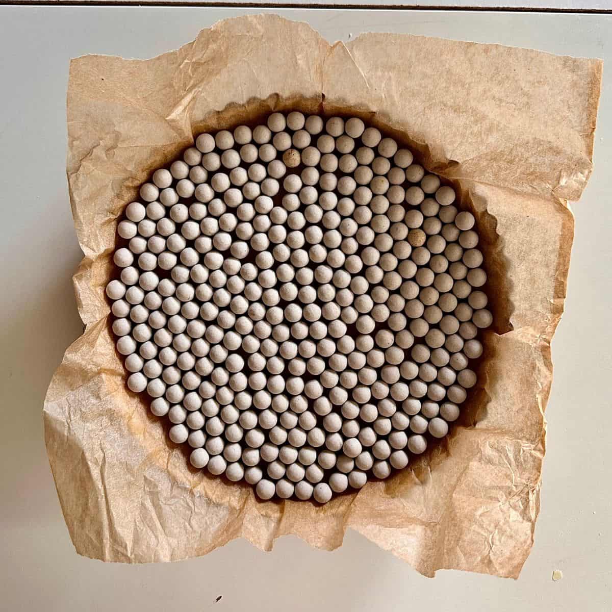 A tart tin containing shortcrust pastry dough, then lined with parchment paper and filled with ceramic baking balls, ready to bake the dough for a beetroot and goats cheese tart.