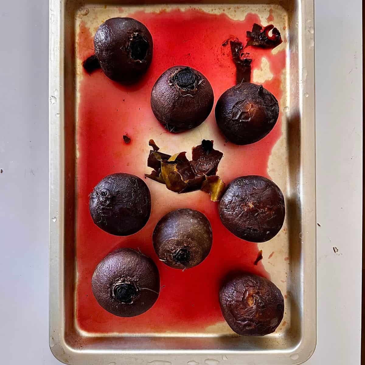 Eight whole red beetroot sat in a baking tray, after cooking. Preparation for a beetroot and goats cheese tart.