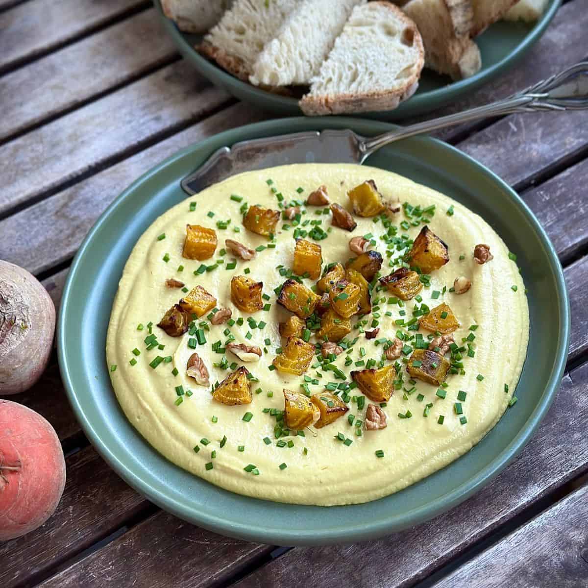 A green plate spread with golden beetroot dip, garnished with small pieces of roasted beetroot and chopped chives.