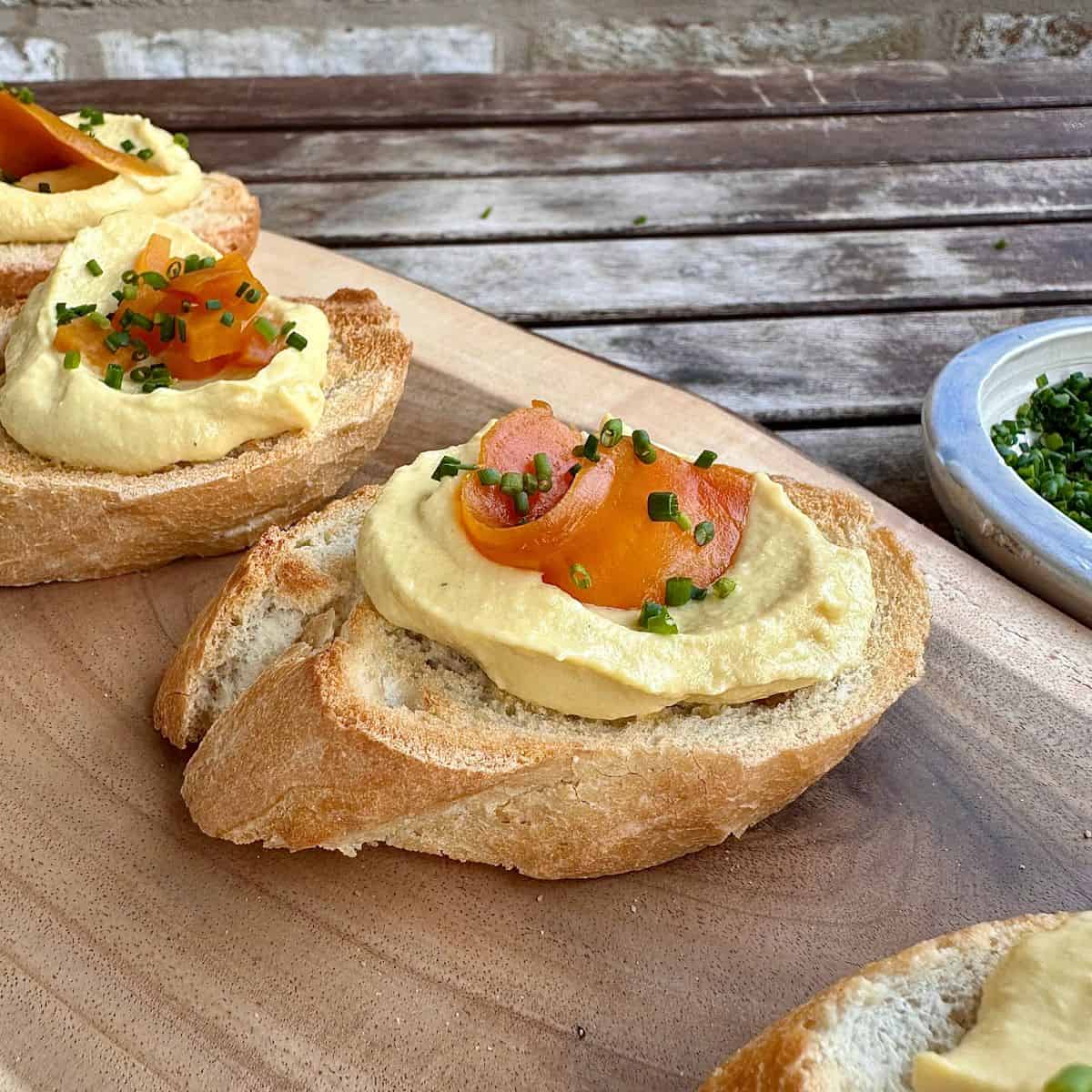 A slice of baguette with beetroot dip on top and garnished with a sliver of roasted golden beetroot and chives.