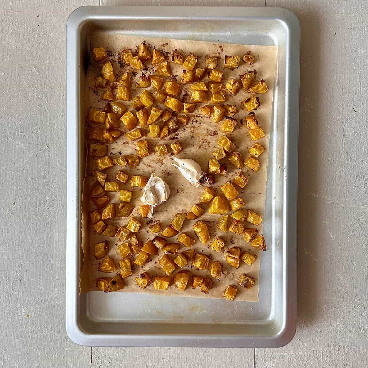 A baking tray containing roasted golden beetroot cut into small dice and also two garlic cloves. For a beetroot dip recipe.
