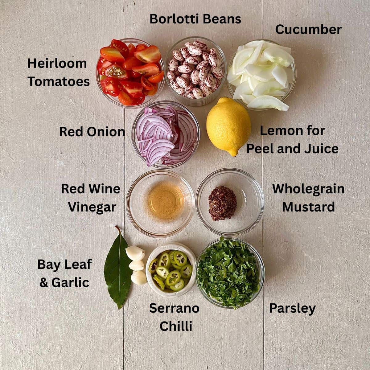 Ingredients for borlotti bean salad in small glass dishes displayed on a white background. The ingredients are annotated.