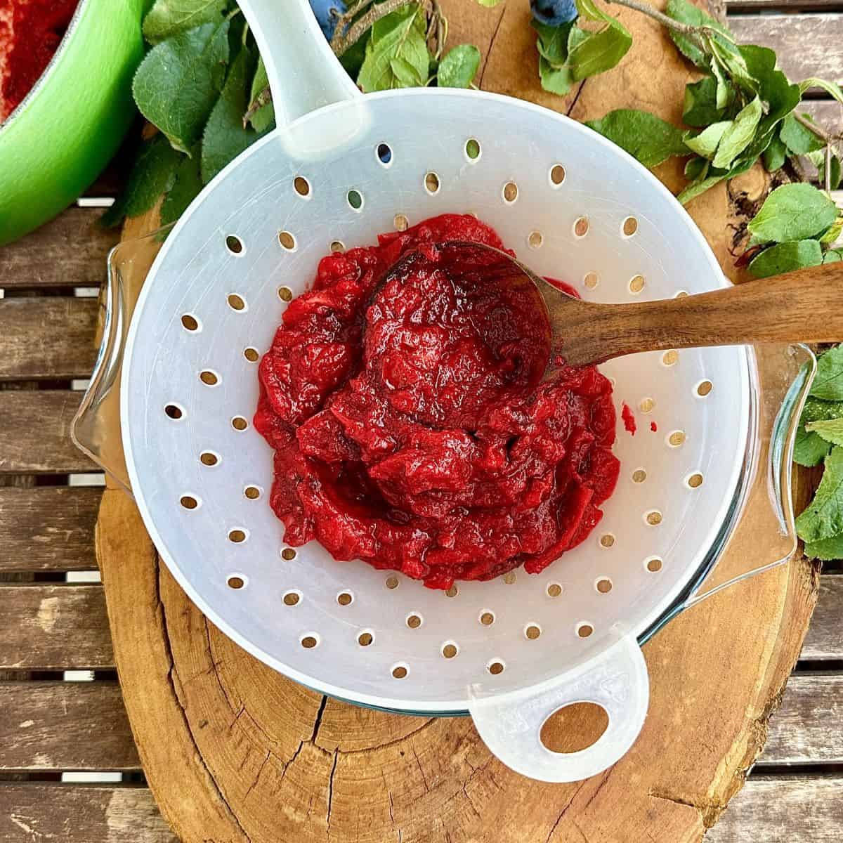 Cooked damsons and crab apples in a colander, with a wooden ladle, ready to press the pulp through to remove pips. For a fruit leather recipe.