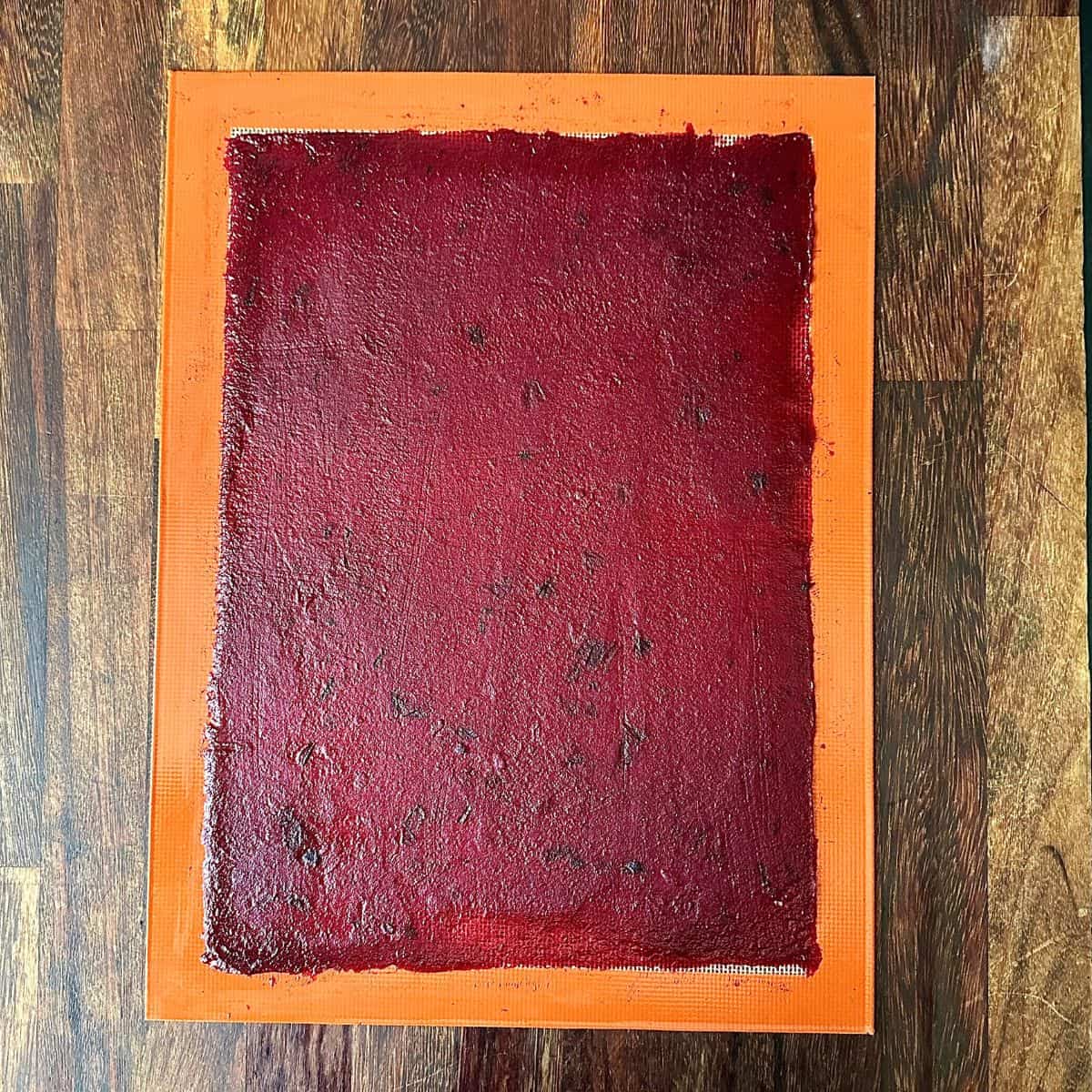 A silicone mat with a thin later of crab apple and damson pulp spread over the mat ready to cook. For a fruit leather recipe.