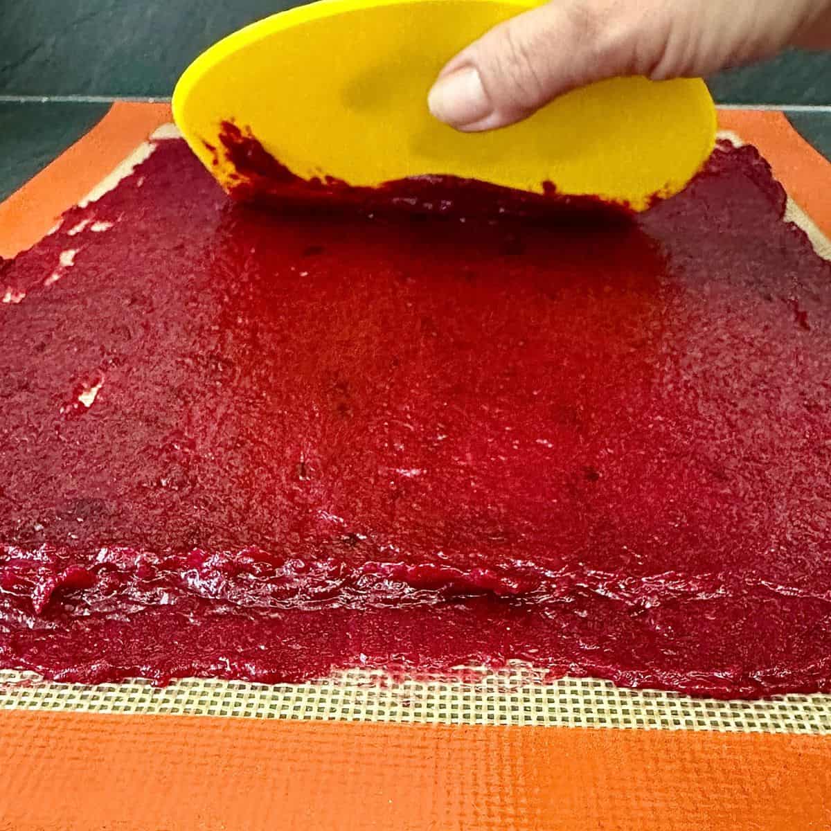 A silicone mat with a thin layer of crab apple and damson pulp, being spread with a plastic spatula. For a fruit apple recipe.