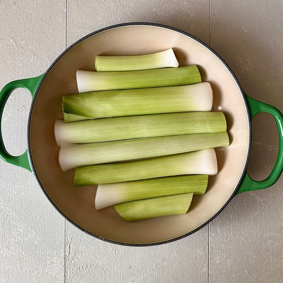 A large green oven-proof dish containing leeks cut to size to fit the bottom. For leek tarte tatin recipe.