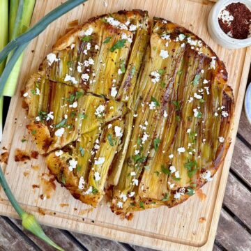 A leek tarte tatin topped with feta and Aleppo pepper flakes sat upon a wooden chopping board.