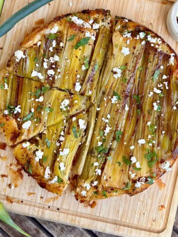 A leek tarte tatin topped with feta and Aleppo pepper flakes sat upon a wooden chopping board.
