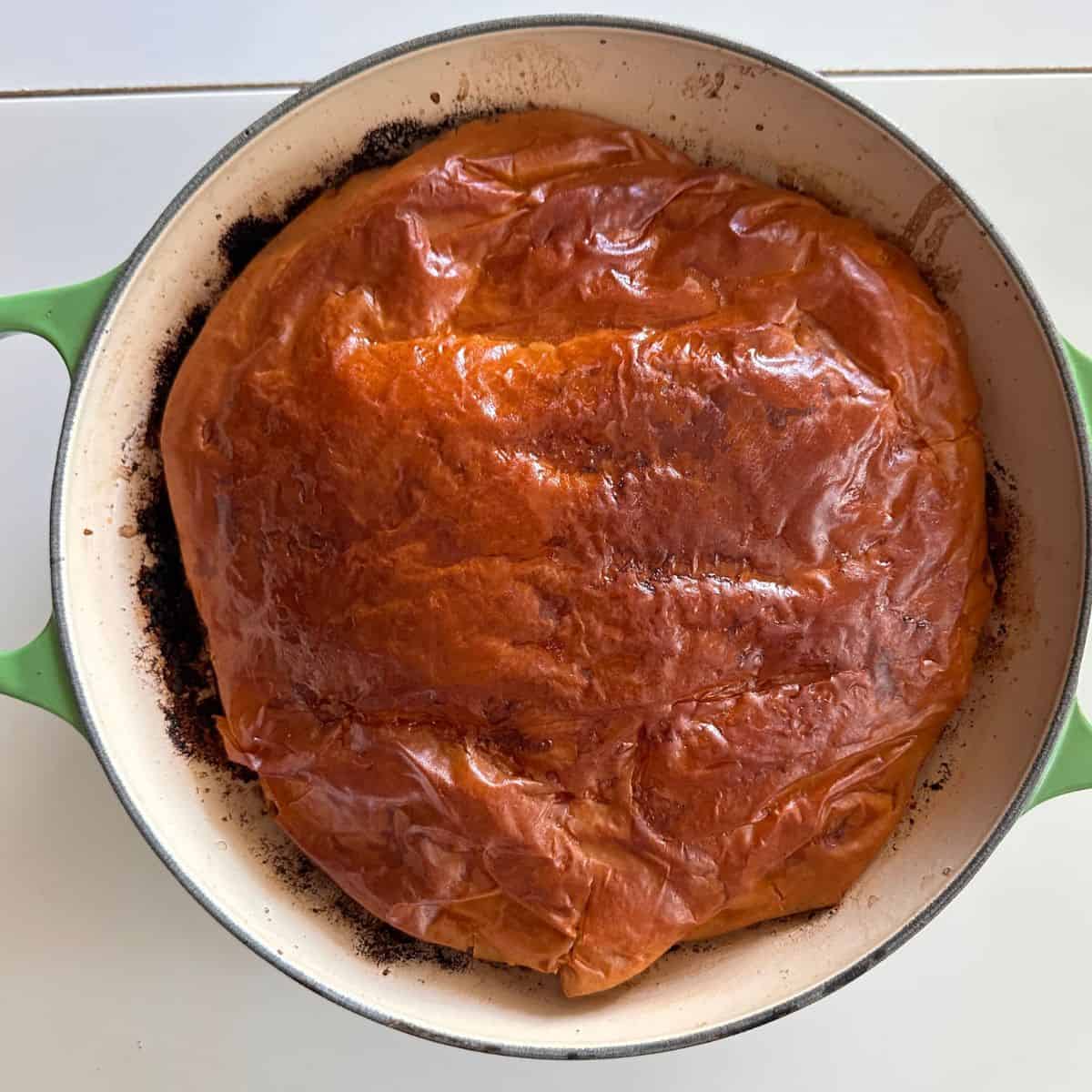 A large green oven-proof dish contains a leek tarte tatin. Showing the filo pasty base after baking - golden and crispy.