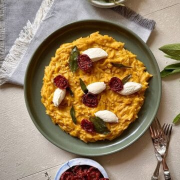 Pumpkin orzo on a green plate, garnished with fried sage leaves, dried cherry tomatoes and soft cheese quenelle.
