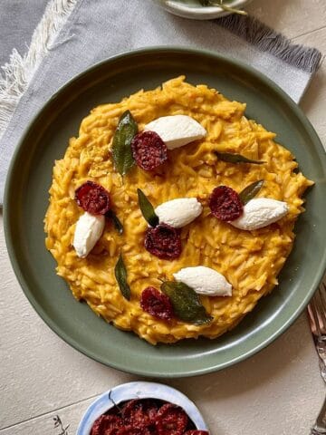 Pumpkin orzo on a green plate, garnished with fried sage leaves, dried cherry tomatoes and soft cheese quenelle.