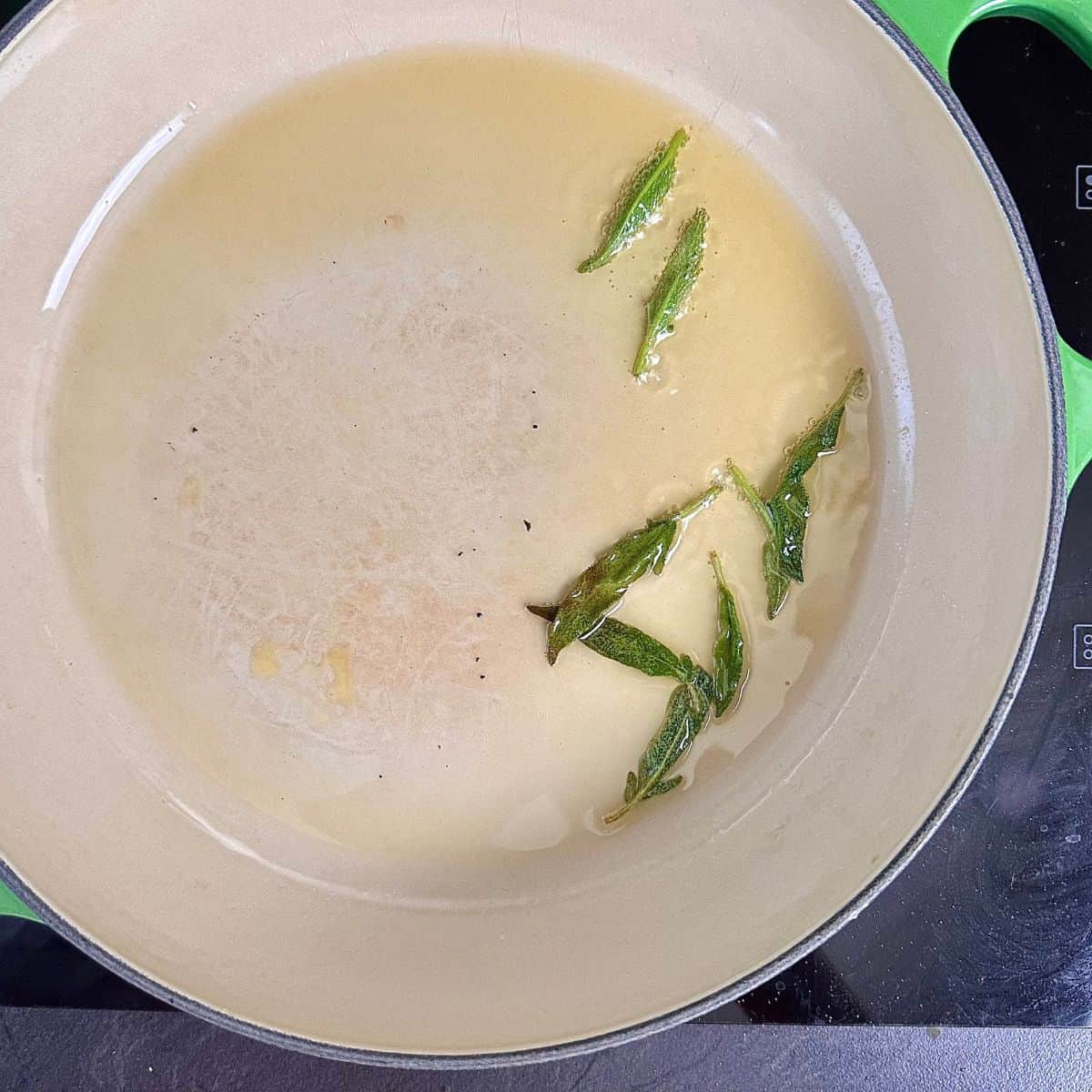 Sage leaves frying in oil in a large pan. For a pumpkin orzo recipe.