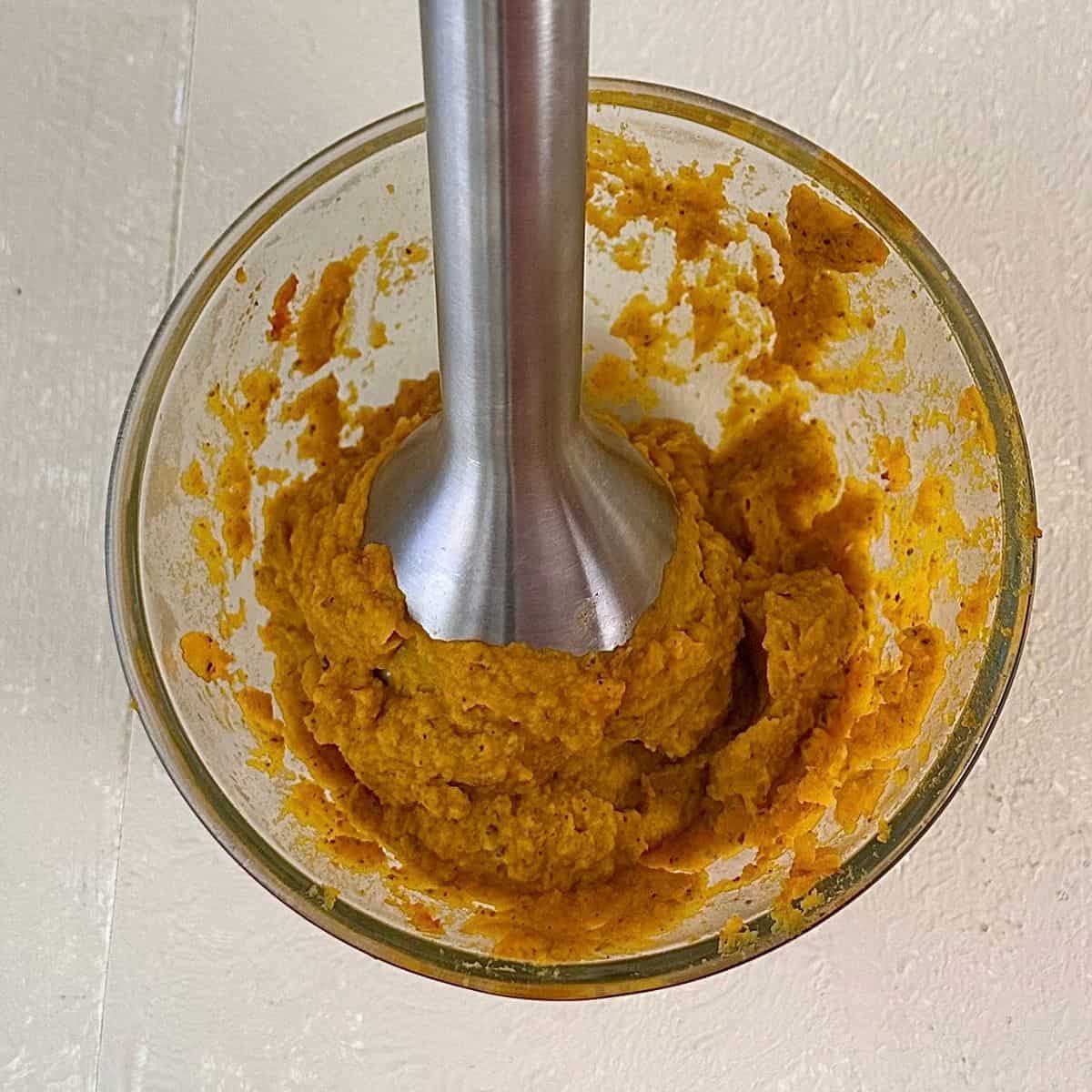 A glass bowl containing pureed crown prince pumpkin. A stick blender is in the puree. For a pumpkin orzo recipe.